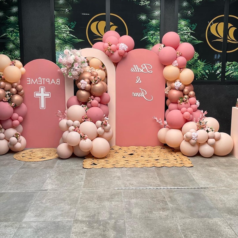 Décoration de baptême rose pêche et or rose avec ballons, arches panneau 'BAPTÊME' et 'Bella & June', fleurs et croix blanche.