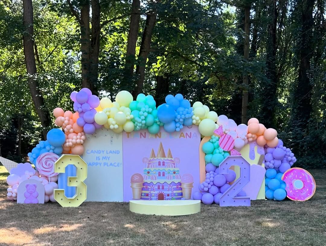 Décoration extérieure pour anniversaire sur le thème Candy Land avec ballons multicolores, chiffres lumineux '3' et '2', et le texte 'CANDY LAND IS MY HAPPY PLACE!' pour TANN NANA.