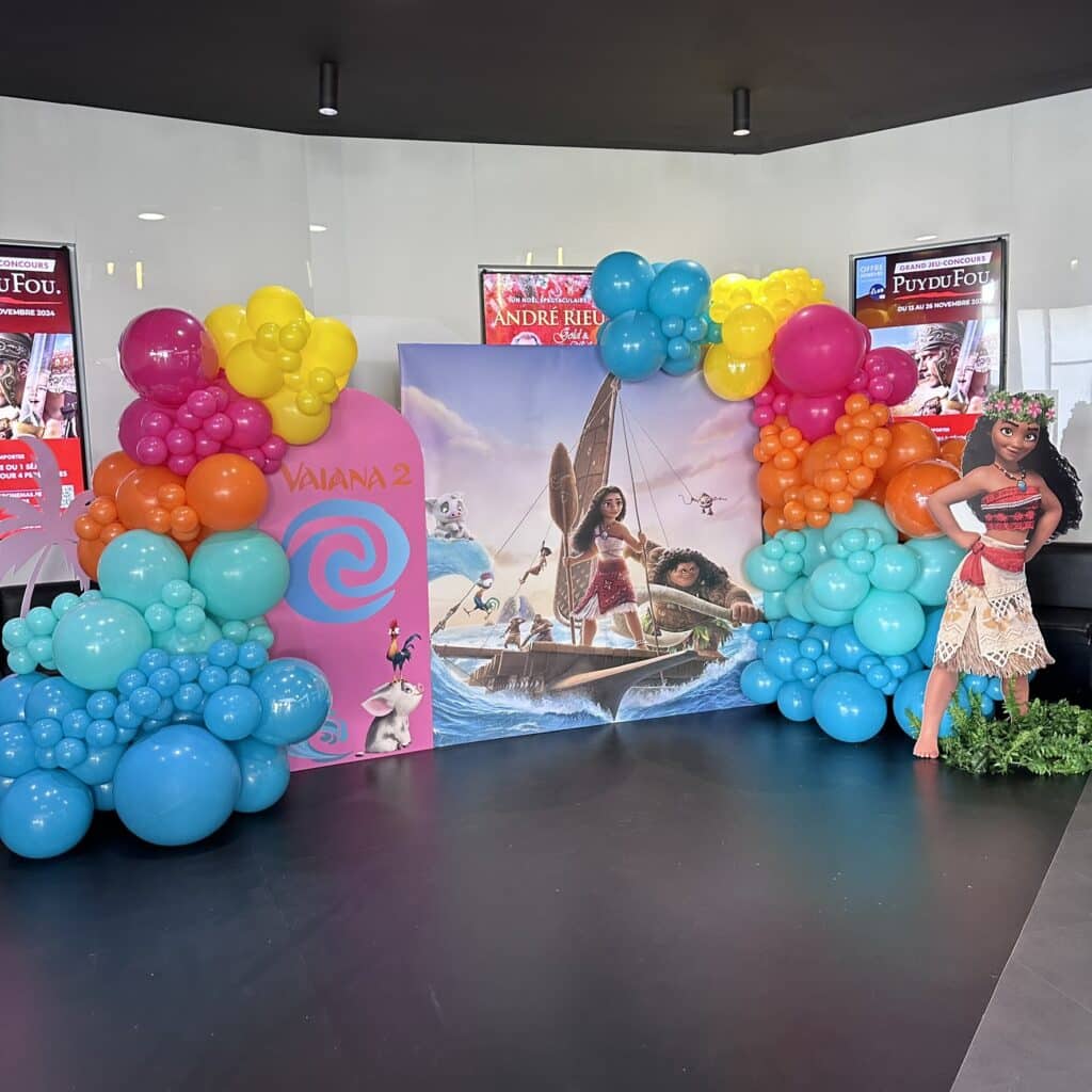 Mur photo Vaiana 2 : ballons éclatants et décor océanique. Décor promotionnel Vaiana 2. Ballons arc-en-ciel, affiche de Moana/Maui sur le bateau et découpe Vaiana grandeur nature.