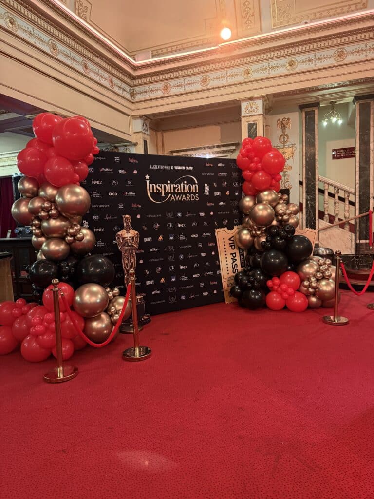 Inspiration Awards : Décoration Événementielle Prestige Décoration Inspiration Awards avec arches de ballons rouges, dorés et noirs, statue dorée sur tapis rouge prestigieux.